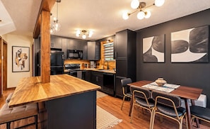 A modern kitchen with dark cabinetry, a wooden island, and a dining area with a table and chairs.