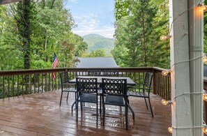A wooden deck with a table and chairs, an American flag, and a view of a mountain range.