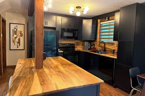 A modern kitchen with dark cabinetry, a wooden countertop, and a built-in microwave.