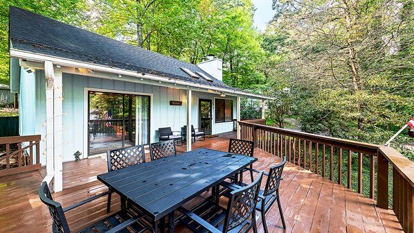 A wooden deck with a table and chairs, a covered patio area, and a view of trees.