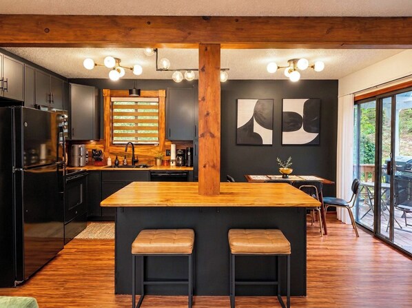 A modern kitchen with a central island, wooden beams, and a large window.