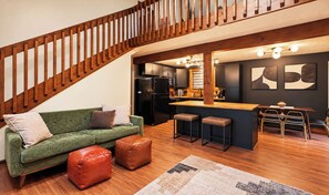 Eine moderne Küche mit einer Holztreppe, einem grünen Sofa, Lederhocker und einer Bar.