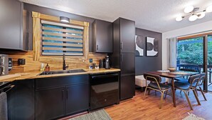 A modern kitchen with dark cabinetry, a wooden backsplash, and a dining area with a table and chairs.