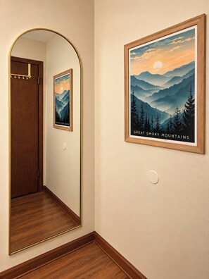 A hallway with a wooden door, a mirror, and a framed picture of the Great Smoky Mountains.