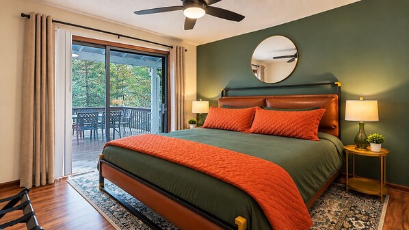 A bedroom with a large bed, a ceiling fan, a round mirror, and a view through a sliding glass door to an outdoor area.