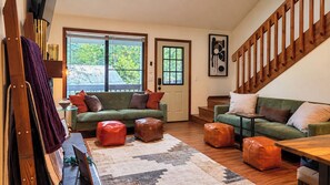 A living room with a sofa, ottomans, a coffee table, and a staircase.