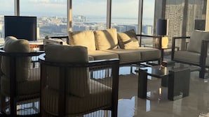 A modern living room with a sofa, armchairs, a coffee table, and a TV. Large windows offer a city view. - Levi & Moon's Home (Pasay)