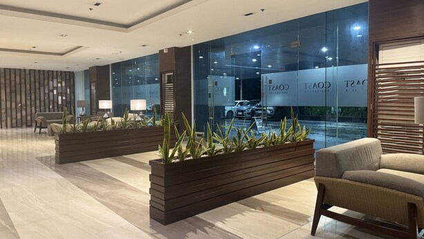 A modern hotel lobby with a seating area, a reception desk, and a glass wall displaying the hotel name. - Levi & Moon's Home (Pasay)