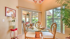 Un coin repas avec une table en verre, des chaises en bois, une petite table d’appoint rouge et une grande fenêtre donnant sur un paysage verdoyant.