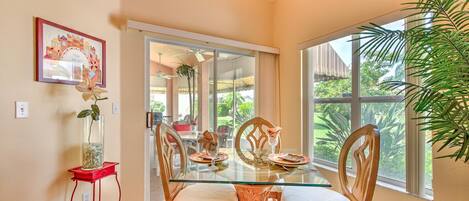 A dining area with a glass table, wooden chairs, a red side table, and a large window offering a view of greenery.