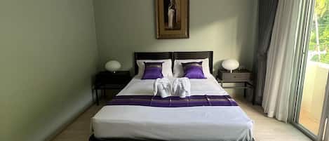 A neatly made bed with a white and purple bedspread, a headboard, and two bedside tables with lamps.