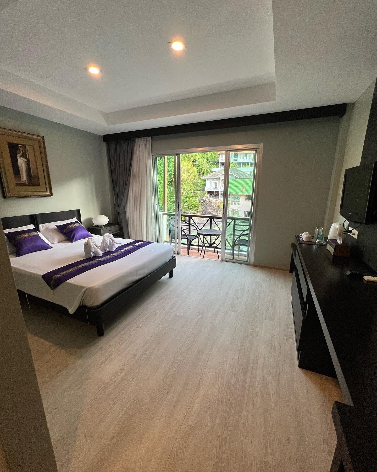 Une chambre d’hôtel équipée d’un lit, d’un bureau, d’une télévision et d’un balcon donnant sur un paysage verdoyant.
