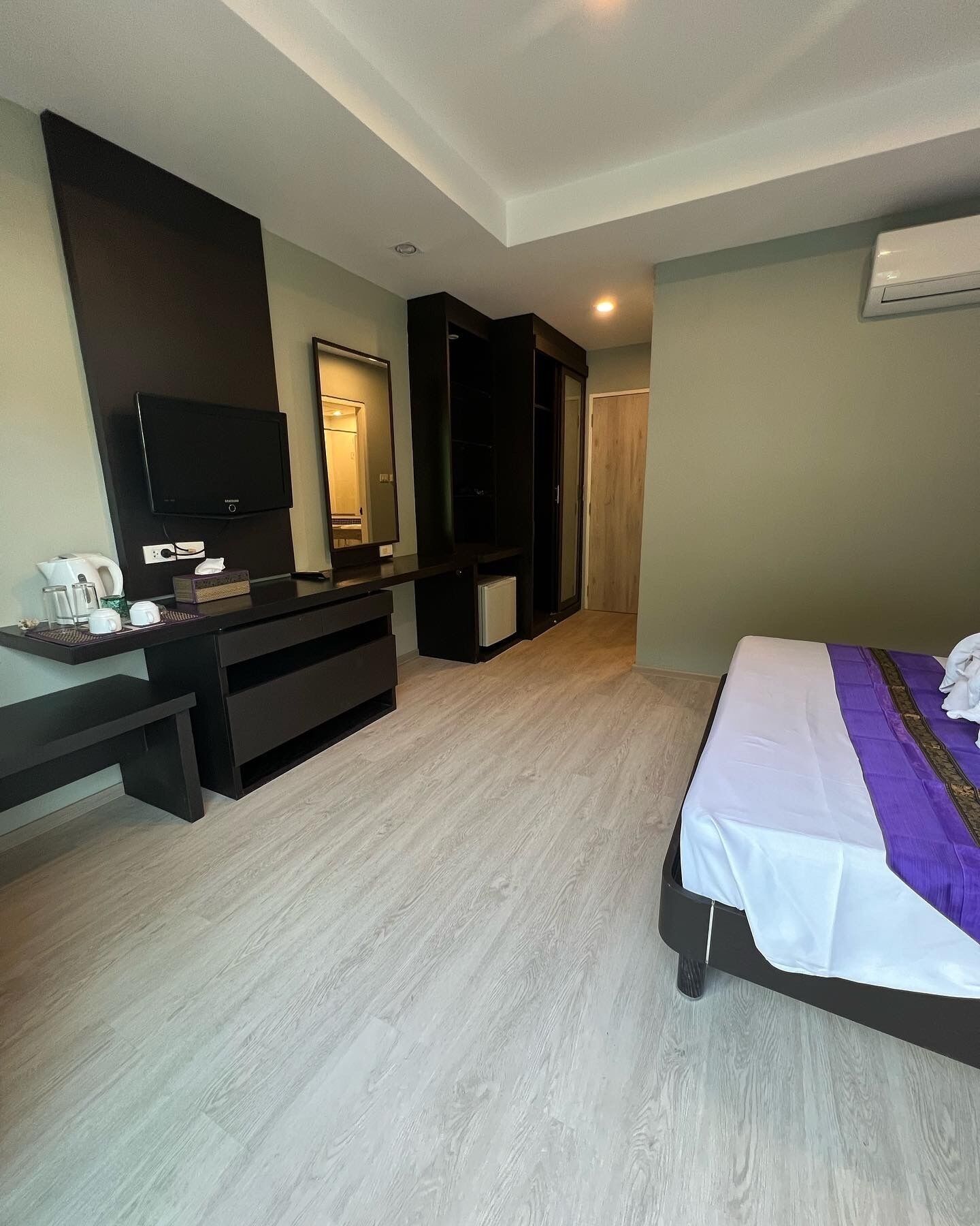 A hotel room with a bed, a TV, a desk with a coffee maker, and a wardrobe.
