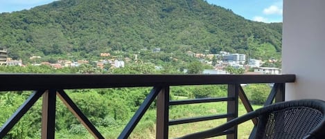 Un balcón con una mesa y una silla, con vista a un paisaje montañoso y edificios a lo lejos.