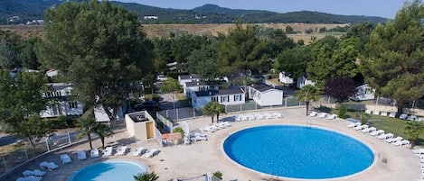 A resort with a large circular pool, multiple lounge chairs, and a view of the surrounding landscape.