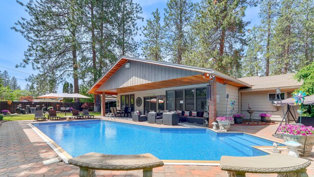 A swimming pool with a covered patio area, outdoor furniture, and a stone bench. - Spokane Valley Escape (Spokane Valley)