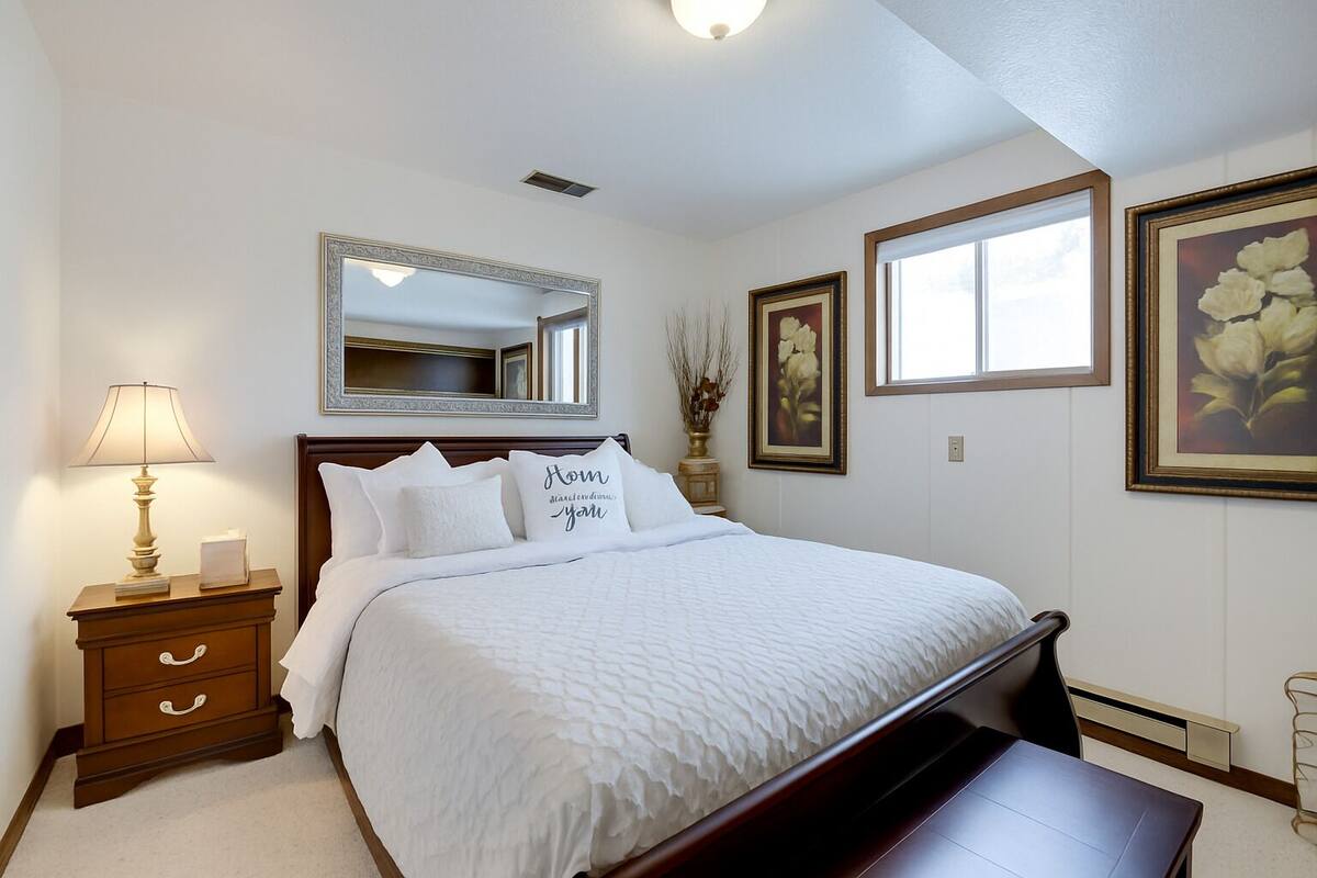 A neatly arranged bedroom with a large bed, bedside tables, a mirror, and framed artwork on the walls.
