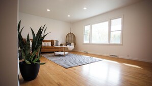 A spacious room with hardwood flooring, a large window, a hanging chair, a sofa, and a potted plant. - Modern 4BR Home on Golf Course + Sauna Close to Campus, Dining & Entertainment (Greencastle)