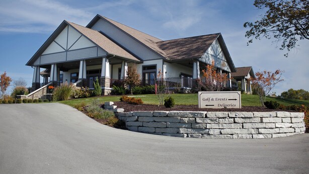 A two-story building with a stone facade and a sign indicating 'Golf & Events' and 'Deliveries'. - Modern 4BR Home on Golf Course + Sauna Close to Campus, Dining & Entertainment (Greencastle)