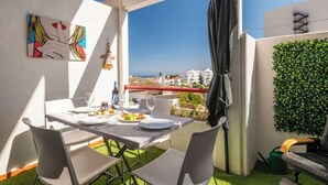 Un coin repas avec une table dressée pour deux personnes, une vue sur la mer et un mur végétal.