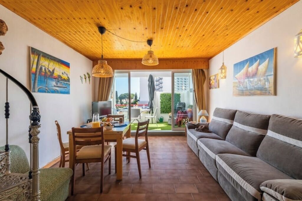 Un salon chaleureux avec un plafond en bois, un canapé, une table à manger avec des chaises et des œuvres d’art accrochées aux murs.