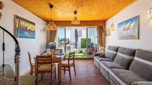 Un salon chaleureux avec un plafond en bois, un canapé, une table à manger avec des chaises et des œuvres d’art accrochées aux murs.