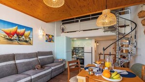 Un salon chaleureux avec un canapé, une table à manger ornée de fruits et une cuisine en arrière-plan.