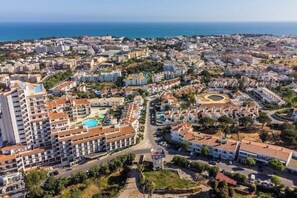 A coastal cityscape with a prominent hotel featuring multiple floors, a swimming pool, and a central courtyard.