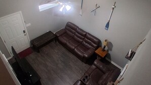 A living room with a brown leather sofa, a wooden coffee table, and a ceiling fan. - Rainwaters Bunkhouse - Close to Crystal Springs and Lake Ouachita
 (Royal)