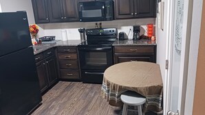 A kitchen with dark cabinets, a microwave, stove, and a coffee maker. - Rainwaters Bunkhouse - Close to Crystal Springs and Lake Ouachita
 (Royal)