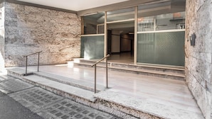 Une entrée moderne, avec des murs en pierre, une porte en verre et une rampe d’appui en métal.