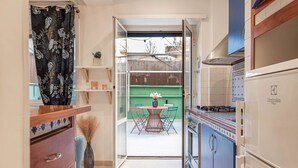 Une cuisine équipée d’une cuisinière, d’un four et de placards. On y trouve une table à manger avec des chaises et un vase rempli de fleurs. La cuisine donne sur un balcon agrémenté d’un mur végétal et offrant une vue sur les bâtiments environnants.