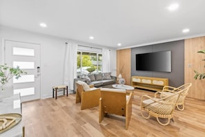A modern living room with a sofa, chairs, a TV, and a wooden floor.