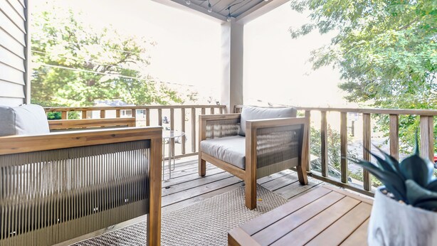 A covered porch with wooden furniture, including a bench and two chairs, and a potted plant.