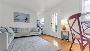 A modern living room with a sofa, a rug, a painting, and a dining area with a chair and table.