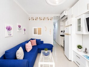 A modern living room with a blue sofa, white cabinets, and a kitchen area with white appliances.