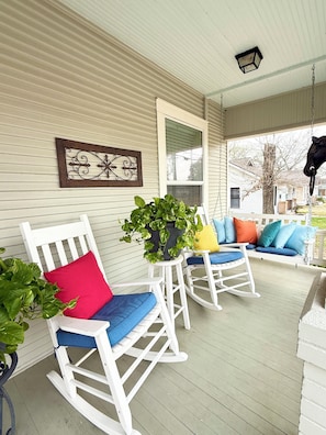 A porch with white rocking chairs, a potted plant, and a hanging lantern.