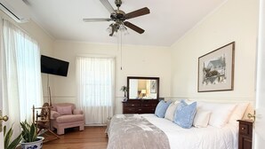 Une chambre à coucher comprenant un lit, un ventilateur de plafond, une commode, un téléviseur et une fenêtre avec des rideaux.
