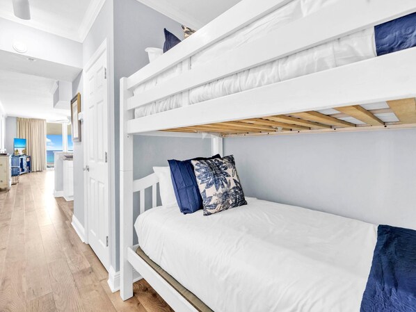 Habitación con literas, ropa de cama blanca y vista al balcón.