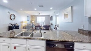 A modern kitchen with granite countertops, stainless steel sink, and white cabinetry. - Sterling Breeze 1207 (Panama City Beach)