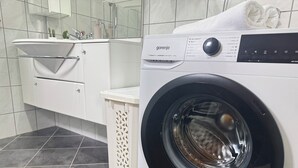 Ein moderner Waschraum mit einer weißen Waschmaschine, einem Waschbecken und einer kleinen Mülltonne.