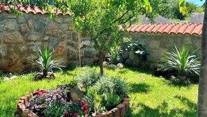 Eine Steinsichtmauer mit einem Ziegeldach, ein grüner Garten mit einem Blumenbeet und ein Baum.