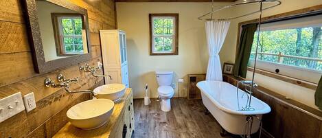 A bathroom with wooden walls, a freestanding bathtub, a double sink vanity, and a toilet.