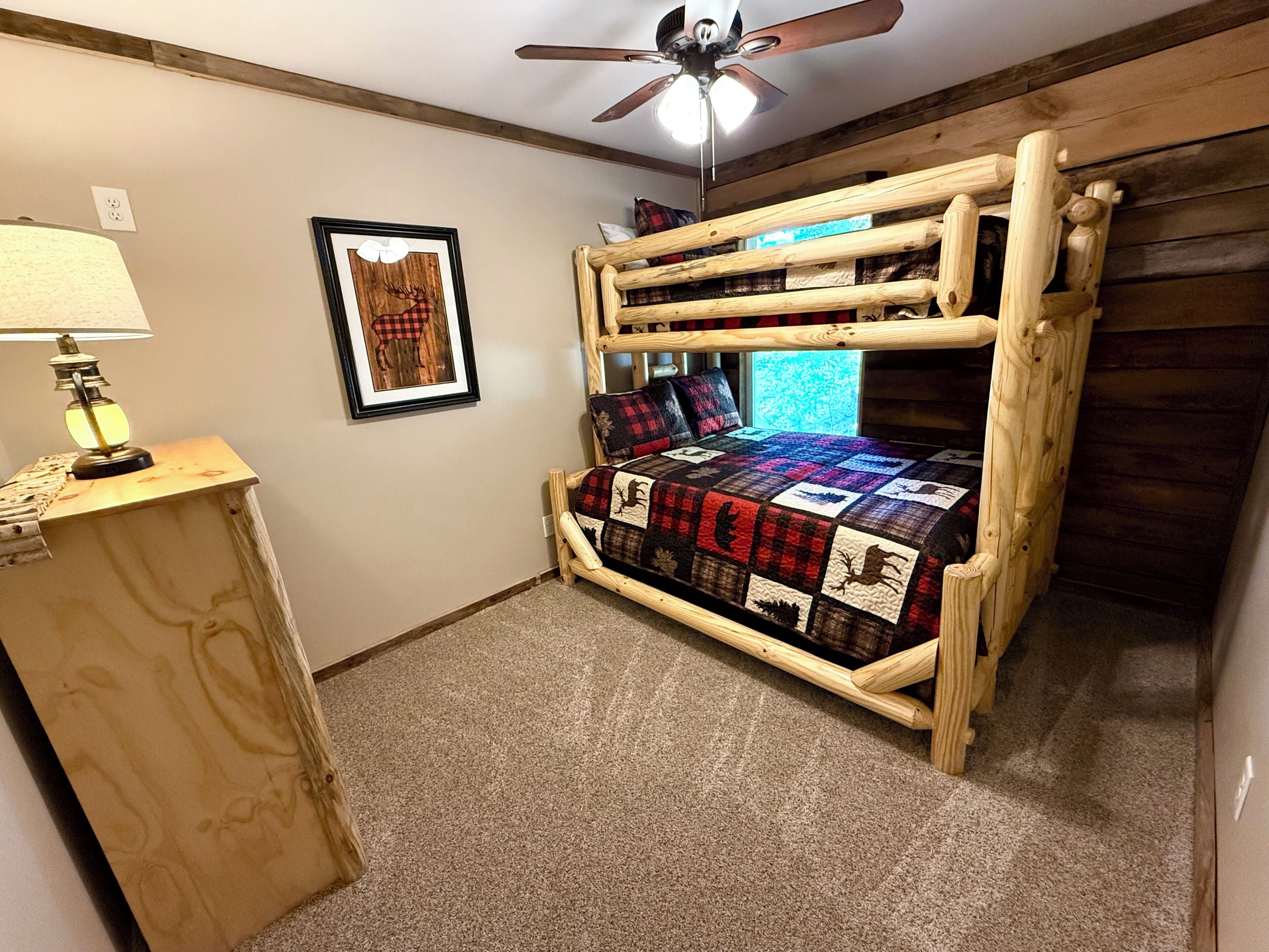 Un letto a castello con una coperta, una scrivania con una lampada e una ventola a soffitto in una stanza con pareti in legno e pavimento rivestito di moquette.