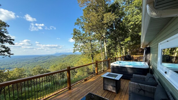 A deck with a hot tub, wicker furniture, and a view of a forested landscape. - Tranquil Escape: Hot Tub, Scenic Views, Family Fun (Ranger)
