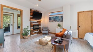 A modern living room with a fireplace, a flat-screen TV, a comfortable sofa, and a dining area. - King Bed | Boho Charm | 2 minutes to Downtown (Eureka Springs)