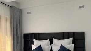A modern hotel room with a large bed, a black headboard, and a window with curtains. - Bamboo-view Breeze Suite (Glenlorne)