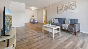 Ein modernes Wohnzimmer mit einem grauen Sofa, einem weißen Couchtisch und einem Flachbildfernseher auf einem weißen Schrank.