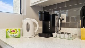 Eine Küchenarbeitsfläche mit Kaffeemaschine, Wasserkocher, einer Packung Lipton Grüntee und einer Teedose.