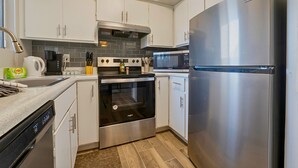 Eine moderne Küche mit weißen Schränken, Edelstahlgeräten, darunter ein Kühlschrank, ein Backofen und eine Mikrowelle, sowie ein Geschirrspüler.